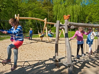 Wingster Waldzoo Kinder spielen auf einem Abenteuer-Spielplatz im Wingster Waldzoo bei Sonnenschein und frischem Grün.
