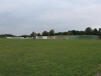Grüne Landebahn mit mehreren Hangars im Hintergrund, umgeben von Bäumen und weitreichendem Himmel.