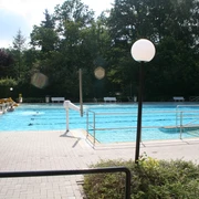 Wiehe-Bad Außenansicht eines großen Freibads mit breitem Wasserbecken, umgeben von grünen Bäumen und Sonnenterrassen.