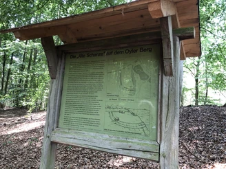 Alte Schanze Oyler Berg Infotafel im Wald mit historischem Plan und Text zur "Alten Schanze" auf dem Oyler Berg im Hintergrund.