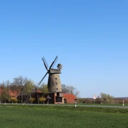 Pottmühle Petershagen Historische Pottmühle Petershagen mit Windmühlenflügeln, umgeben von roten Gebäuden und grüner Landschaft.