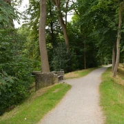 Ein schmaler, von grünen Bäumen gesäumter Weg auf einer historischen Wallanlage führt durch ein bewaldetes Gebiet.