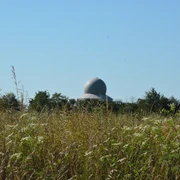 Radarstation Auenhausen: Eine moderne Kuppel hebt sich hinter einer Wiese mit Gräsern und Wildblumen ab.