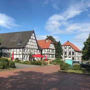 Gehrden Fachwerkhäuser in Gehrden mit roten Sonnenschirmen, umgeben von Bäumen unter einem blauen Himmel.