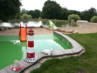 Naturfreibad Pennigsehl Naturfreibad Pennigsehl mit rutschender Kinderrutsche, Leuchtturm-Skulpturen und grünem Rasen.