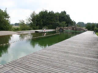 Naturfreibad Pennigsehl Ein Naturfreibad mit hölzernem Steg, umgeben von Bäumen, lädt zur Erholung und zum Eintauchen ein.