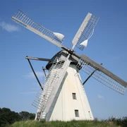 Windmühle Großenheerse Eine weiße Holländerwindmühle mit Holzflügeln erhebt sich majestätisch vor einem klaren blauen Himmel.