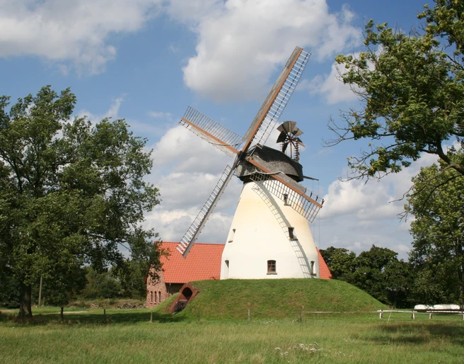 Windmühle Heimsen Windmühle Heimsen mit rotem Dach und großen Flügeln umgeben von Bäumen unter blauem Himmel.