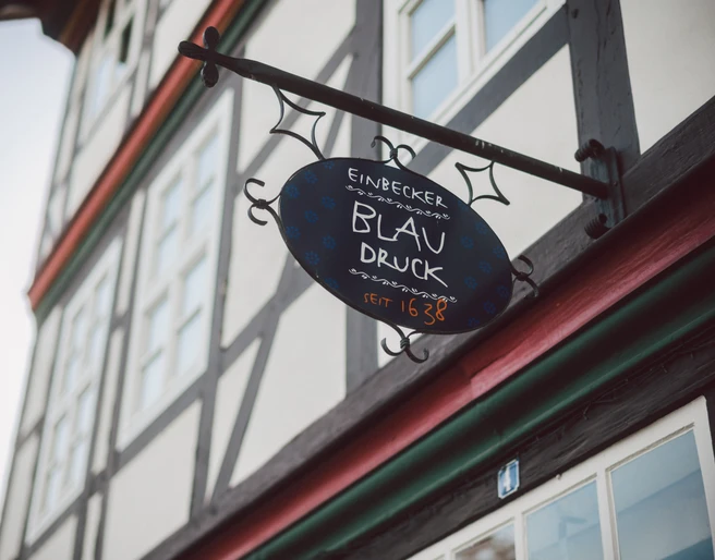 Beschilderung „Einbecker Blaudruck 1638" an einem Fachwerkhaus.