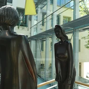 Zwei moderne Bronze-Skulpturen stehen sich gegenüber in einem lichtdurchfluteten Gebäudekomplex.