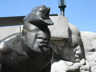 Skulptur "Zigarrenmacher" Bronzeskulptur eines Zigarrenmachers mit markantem Gesichtsausdruck und drei umstehenden Figuren.