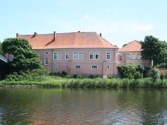 Schloß Hoya Historisches Schloß Hoya am Ufer eines Flusses, umgeben von Bäumen unter blauem Himmel.