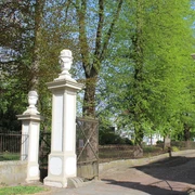 SG Grafschaft Hoya Rittergut von Behr  Eingang des historischen Ritterguts von Behr, gesäumt von Säulen mit dekorativen Vasen in ländlicher Umgebung.