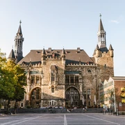 Aachener Rathaus auf Katschhof mit prächtiger Fassade aus Bruchstein, umgeben von alten Bäumen und historischer Architektur.