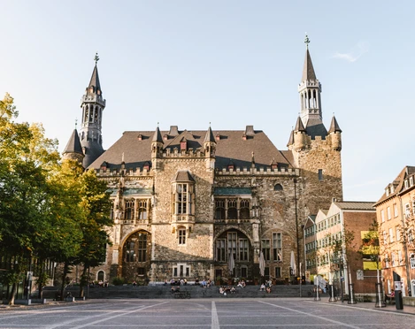 Aachener Rathaus auf Katschhof mit prächtiger Fassade aus Bruchstein, umgeben von alten Bäumen und historischer Architektur.