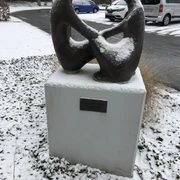 Skulptur "Das Gespräch" Skulptur "Das Gespräch", bedeckt mit Schnee, steht auf einem Sockel in verschneiter Umgebung.