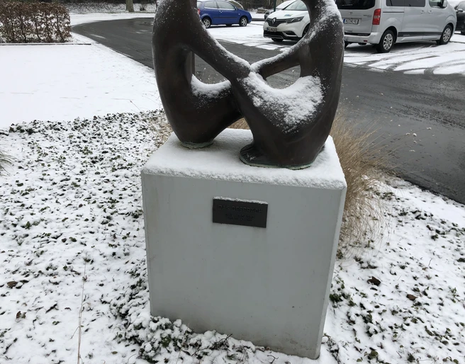 Skulptur "Das Gespräch" Skulptur "Das Gespräch", bedeckt mit Schnee, steht auf einem Sockel in verschneiter Umgebung.
