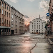 Blick über eine breite, nasse und von mehrstöckigen Gebäuden begleitete Straße auf das Theater Aachen und den Sonnenuntergang im Hintergrund.