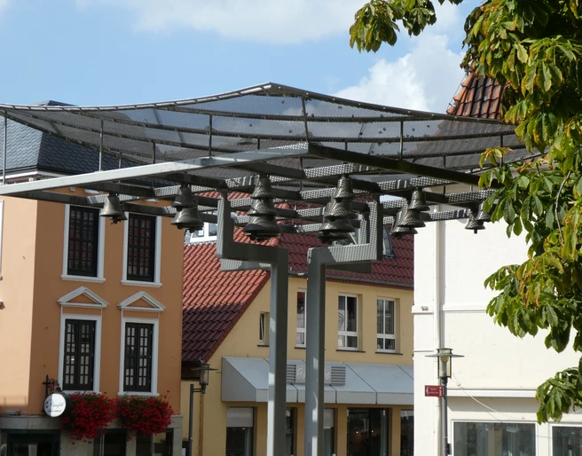 Achimer Glockenspiel Ein modernes Glockenspiel mit mehreren Glocken vor historischen Stadthäusern in Achim bei sonnigem Wetter.