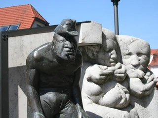 Skulptur Zigarrenmacher Bronzeskulptur eines Zigarrenmachers und Kindern in rustikaler Straßenszene mit roten Ziegeldächern.