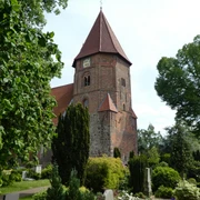 Backsteinkirche mit markantem Turm und rotem Dach, umgeben von gepflegtem Grün und Baumbestand.