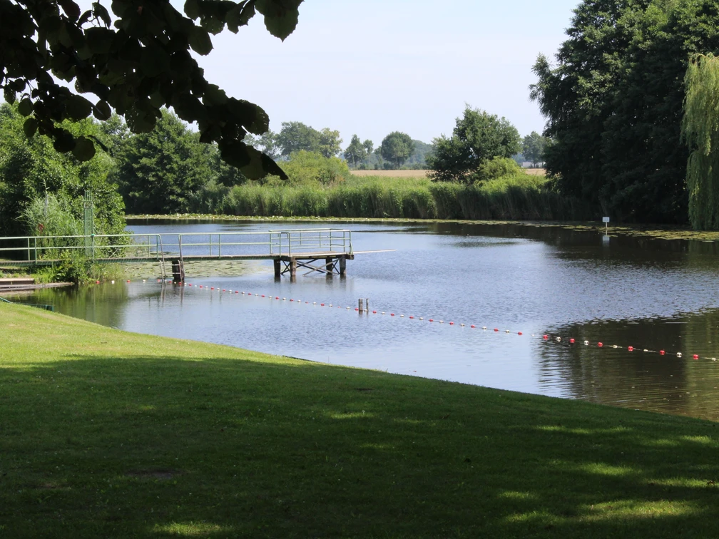 Badestelle Blender See Badestelle am Blender See mit Steg, umgeben von grüner Wiese und Bäumen, lädt zum Entspannen ein.