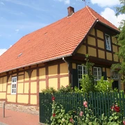 Münchhausenhof in Stolzenau Fachwerkhaus mit roten Ziegeln, umgeben von Rosensträuchern und grünem Zaun unter blauem Himmel.