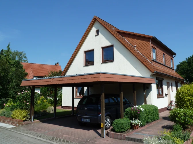 Einfamilienhaus mit Carport und gepflegtem Garten, unter blauem Himmel in ruhiger Umgebung.