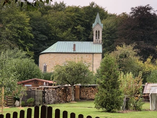 Eine Kapelle steht malerisch inmitten von Bäumen, mit einem kleinen Turm und grünem Dach.