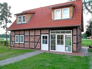 Fachwerkhaus mit rotem Ziegeldach und weißen Fenstern, umgeben von grünem Landschaftsambiente.