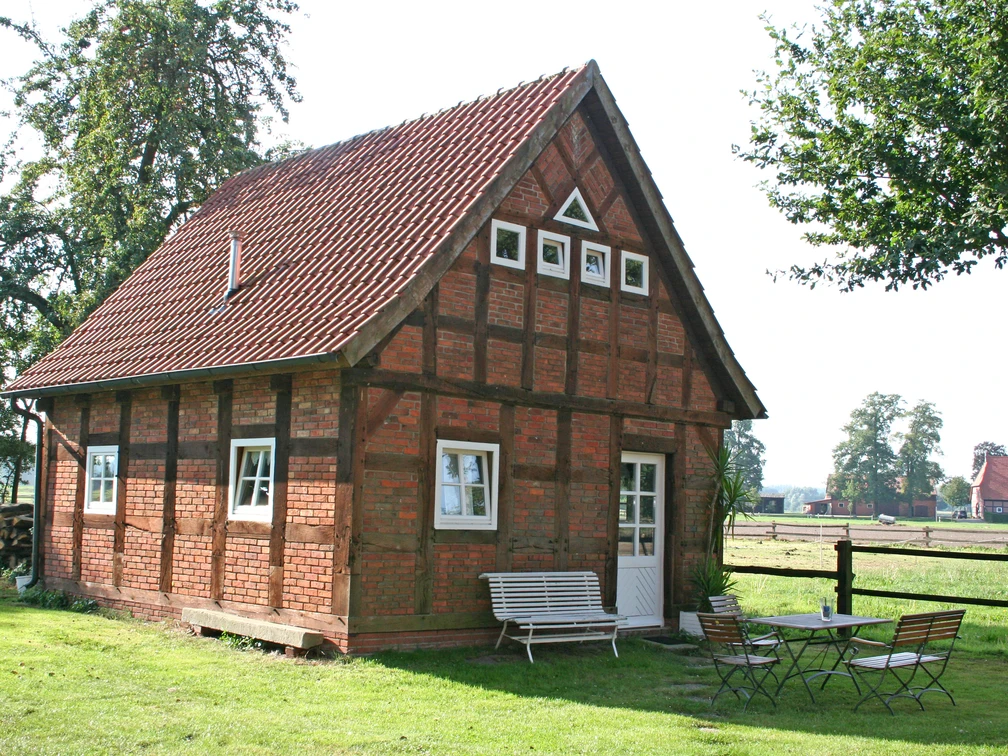 Ferienhof Wikner Fachwerkhaus auf einem grünen Hof mit Gartenmöbeln, umgeben von Bäumen und ländlicher Landschaft.