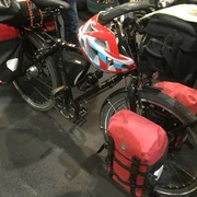 Fahrrad mit Fahrradtasche Ein schwarzes Touringrad mit roter Fahrradtasche und Helm steht gepackt auf einem Boden aus grauem Asphalt.