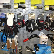 Fahrradzubehör Verschiedene Fahrradhandschuhe in vielfältigen Stilen und Größen hängen an einer perforierten Wand.