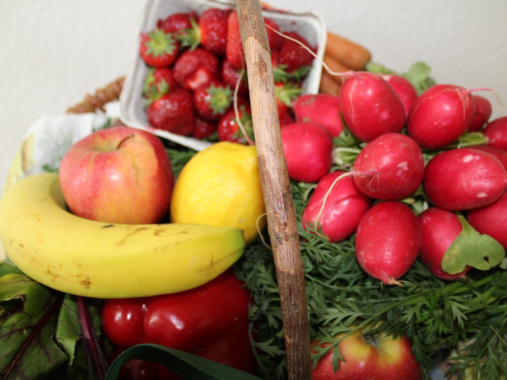 Obst und Gemüse Frisches Obst und Gemüse arrangiert in einem Korb, darunter Banane, Erdbeeren, Radieschen.