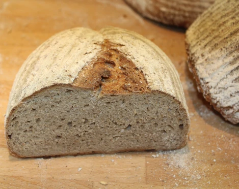 Brot Halbiertes, krustenbetontes Brot auf einem Holzbrett mit feinem Mehl bestäubt.