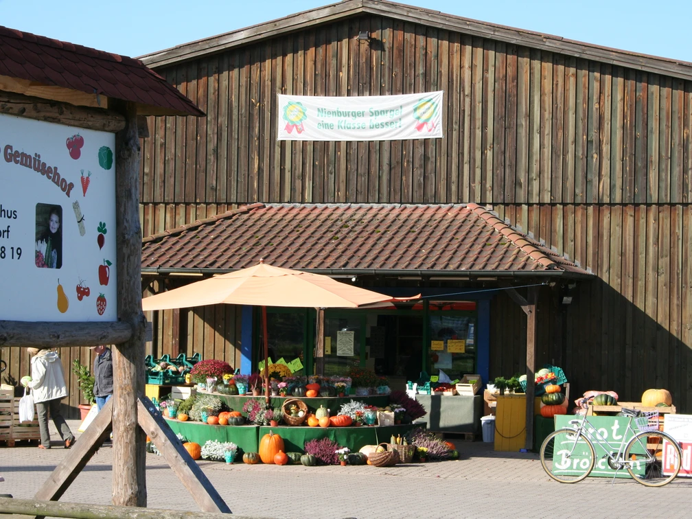 Hofladen Holthus Hofladen Holthus bietet frisches Gemüse und Blumen vor einem rustikalen Holzgebäude mit Schildern.