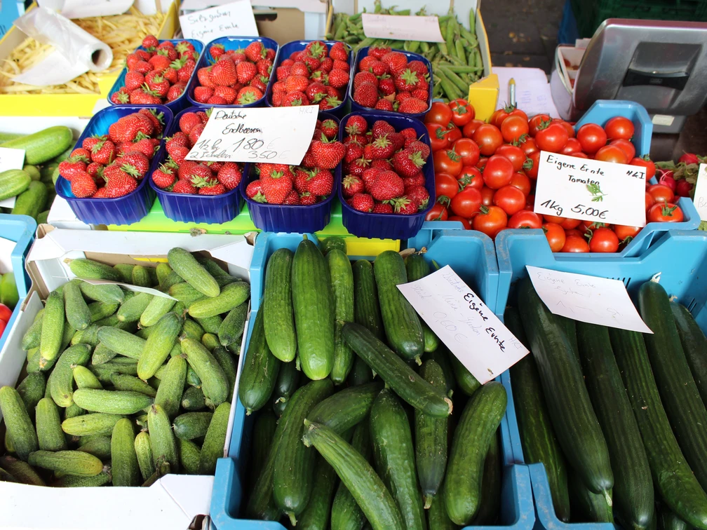 Eine bunte Auswahl frischer Gurken, Tomaten und Erdbeeren, ordentlich auf einem Markt präsentiert.
