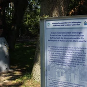 Dörverden Kalibergbau Hülsen Informationstafel zum Kalibergbau in Hülsen, umgeben von Bäumen und einem Ziegelgebäude im Hintergrund.
