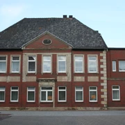 Historisches Backsteingebäude mit symmetrischer Fassade, zehn Fenstern und einem Eingang auf Kiesweg.