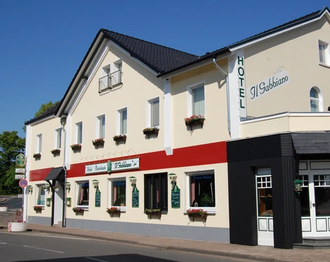 Hotel Il Gabbiano Gelb gestrichenes Hotel mit rotem Detail, großen Fenstern, und Eingang unter blauem Himmel.