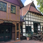 Fachwerkhaus mit roten Dachziegeln, grünumrahmten Fenstern und Restaurant-Schriftzug, umgeben von Bäumen.