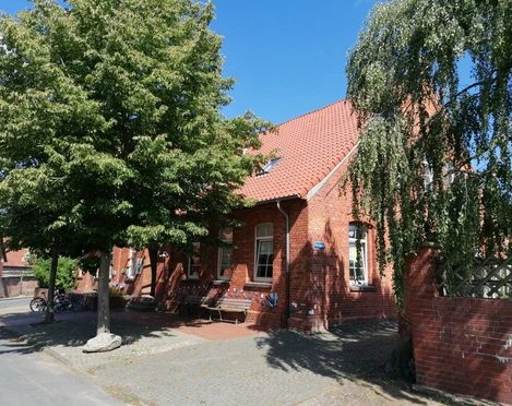 Alte Schule Drakenburg Rotes Backsteingebäude mit Tradition, umgeben von Bäumen, blauer Himmel im Hintergrund, Fahrräder seitlich.