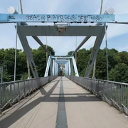 Locust bridge Fußgängerbrücke mit stählernen Trägern und künstlerischem Graffiti, umgeben von grüner Landschaft.Pedestrian bridge with steel girders and artistic graffiti, surrounded by a green landscape.