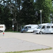 Wohnmobilstellplatz Steimbke Drei Wohnmobile parken auf einem gepflasterten Platz umgeben von hohen Bäumen bei Tageslicht.