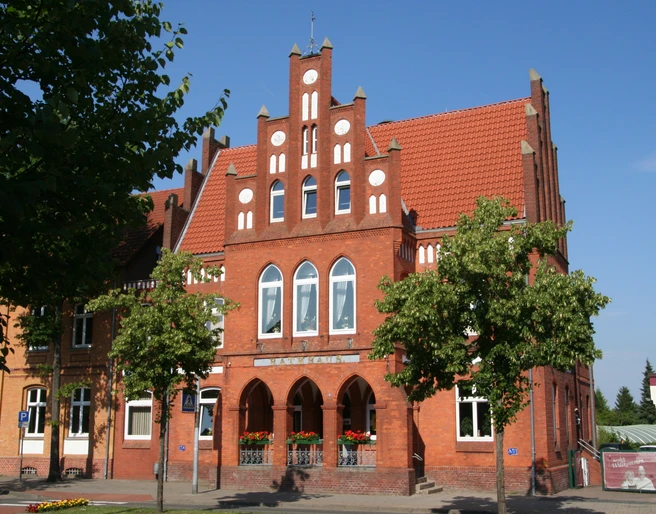 Rathaus Stolzenau Rotes Backsteingebäude mit markantem Stufengiebel, umgeben von Bäumen und blauem Himmel.