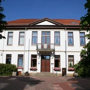 Rathaus Thedinghausen Das zweigeschossige, weiße Rathaus mit rotem Ziegeldach und zentralem Eingang ist von Bäumen umgeben.