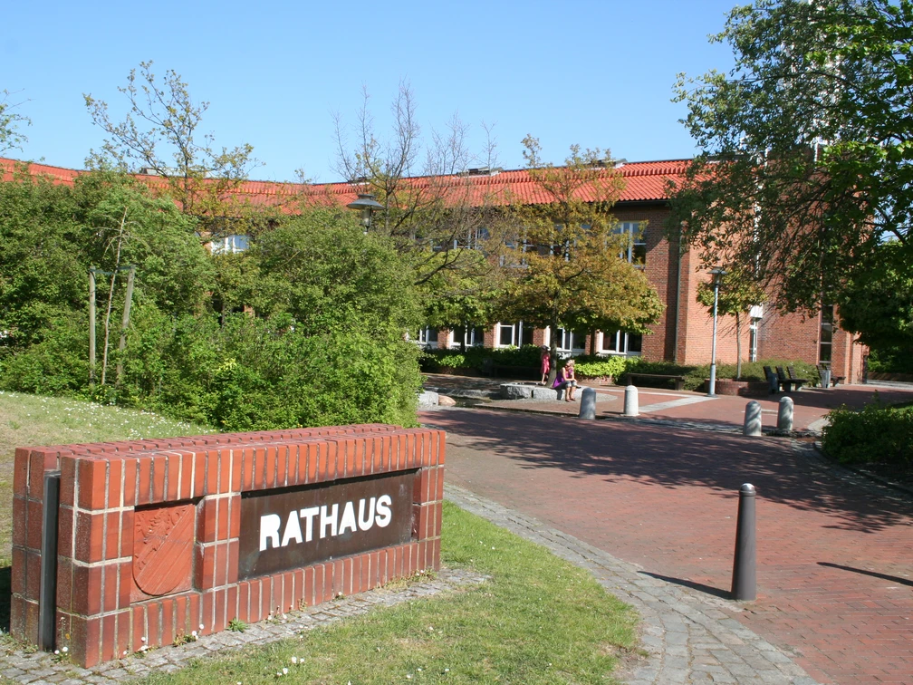 Backsteinbau des Rathauses Weyhe mit rotem Dach, umgeben von grünen Bäumen und blühenden Sträuchern.