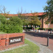 Backsteinbau des Rathauses Weyhe mit rotem Dach, umgeben von grünen Bäumen und blühenden Sträuchern.