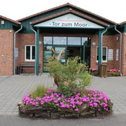 Eingang des Informationszentrums "Tor zum Moor" mit Blumenbeet im Vordergrund und Backsteinfassade.