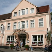 Hotelgebäude mit rosafarbener Fassade und weiß umrahmten Fenstern, vor dem Fahrräder stehen.
